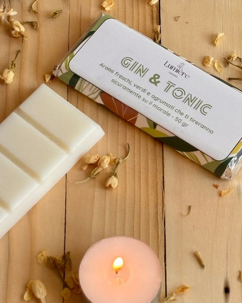 Barretta GinTonic Lumière Essence su piano in legno e una piccola candelina