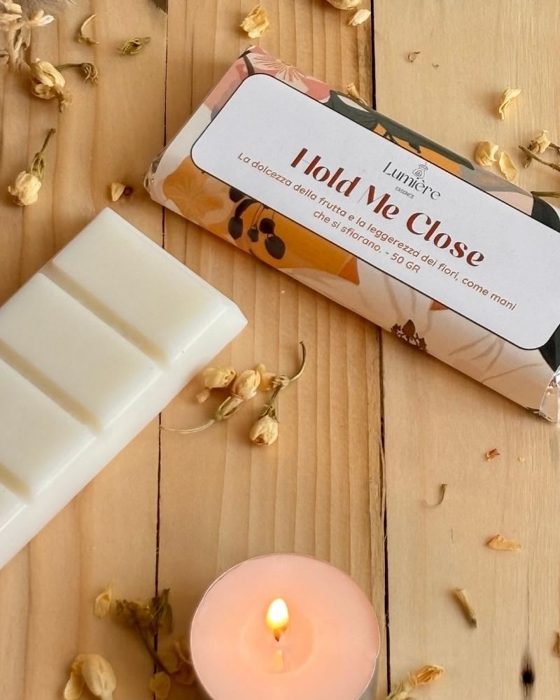 Barretta in cera naturale di cocco profumata per ambiente Hold Me close lumière essence vista da viicino con piccoli fiori decorativi e una candelina accesa affianco
