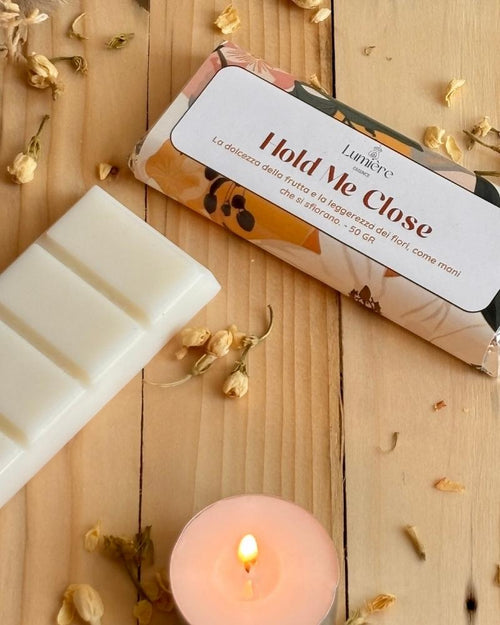 Barretta in cera naturale di cocco profumata per ambiente Hold Me close lumière essence vista da viicino con piccoli fiori decorativi e una candelina accesa affianco