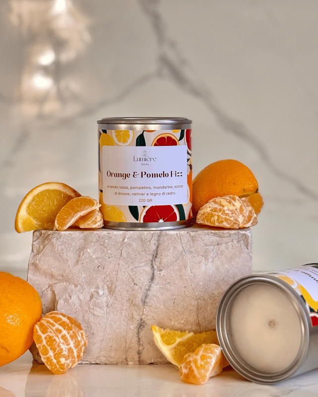 Candela realizzata in cera di cocco naturale cera di cocco, un barattolo di latta  su pietra di marmo sullo sfondo arance pompelmi mandarino, e una candela che mostra l'interno della del barattolo