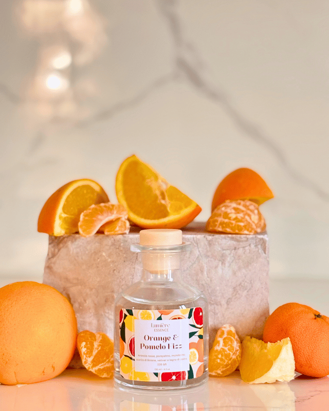 Diffusore a bastoncino in bottiglietta di vetro sullo sfondo una pietra di marmo e agrumi che rappresentano la fragranza