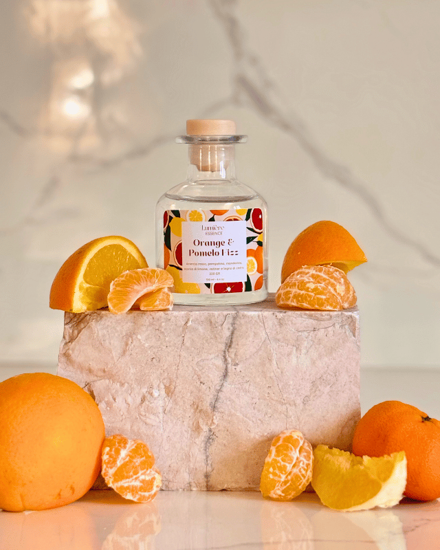 Diffusore a bastoncino in bottiglietta di vetro su pietra di marmo e agrumi che rappresentano la fragranza