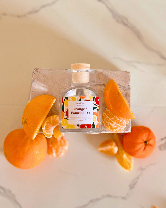 Diffusore a bastoncino in bottiglietta di vetro su pietra di marmo e agrumi che rappresentano la fragranza vista dall'alto
