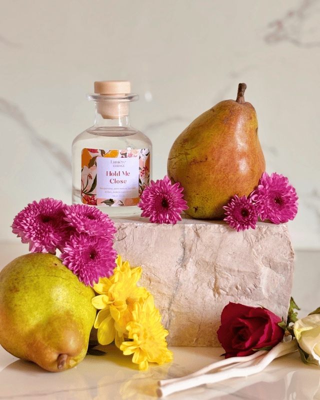 Diffusore a bastoncino in bottiglietta di vetro sullo sfondo pere, fiori e una pietra in marmo