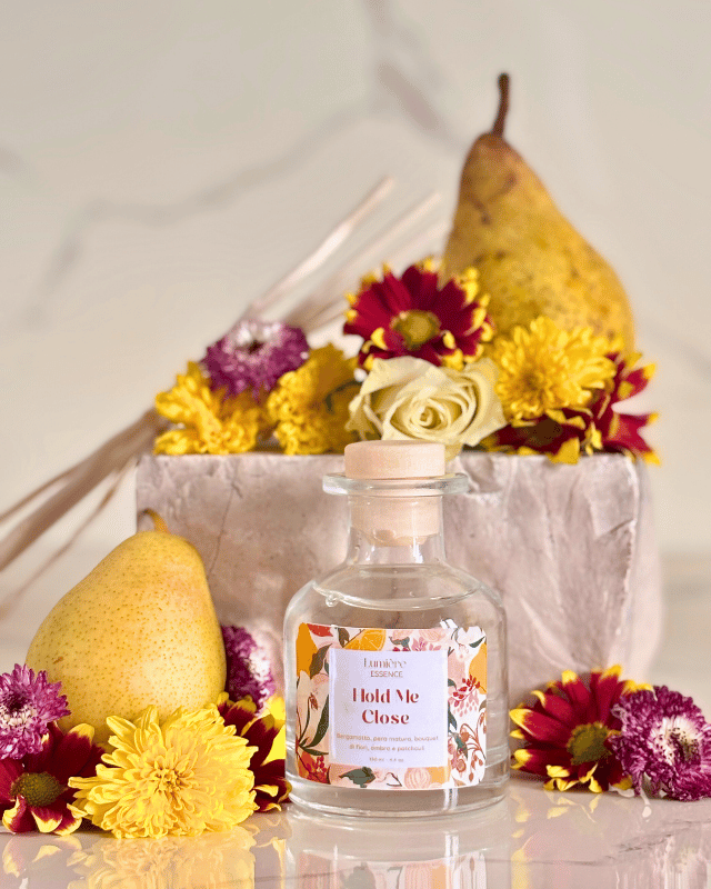 Diffusore a bastoncino in bottiglietta di vetro sullo sfondo pere, fiori e una pietra in marmo