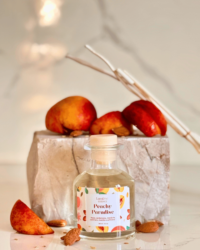 Diffusore per ambiente a bastoncino in bottiglietta di vetro sullo sfondo pietra di marmo e pesche che rappresentano la fragranza