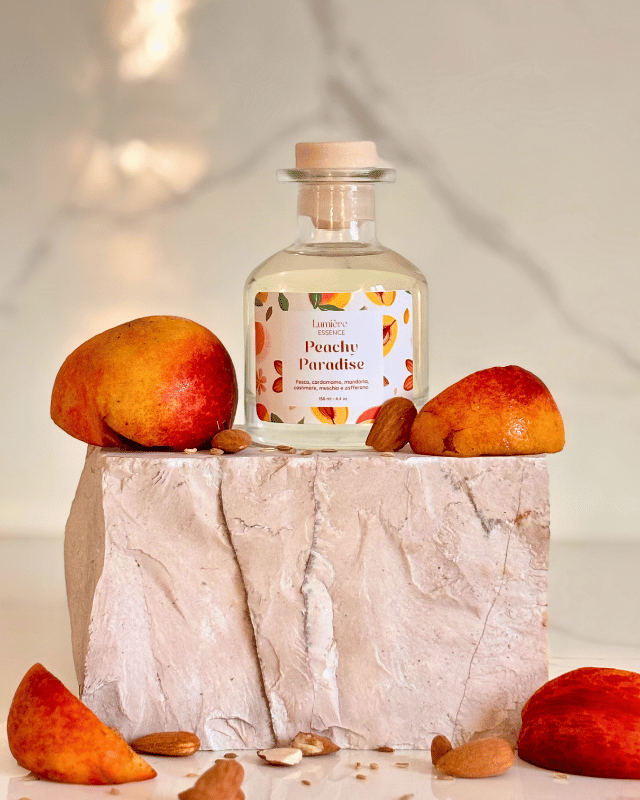 Diffusore per ambiente a bastoncino in bottiglietta di vetro su pietra di marmo e pesche che rappresentano la fragranza