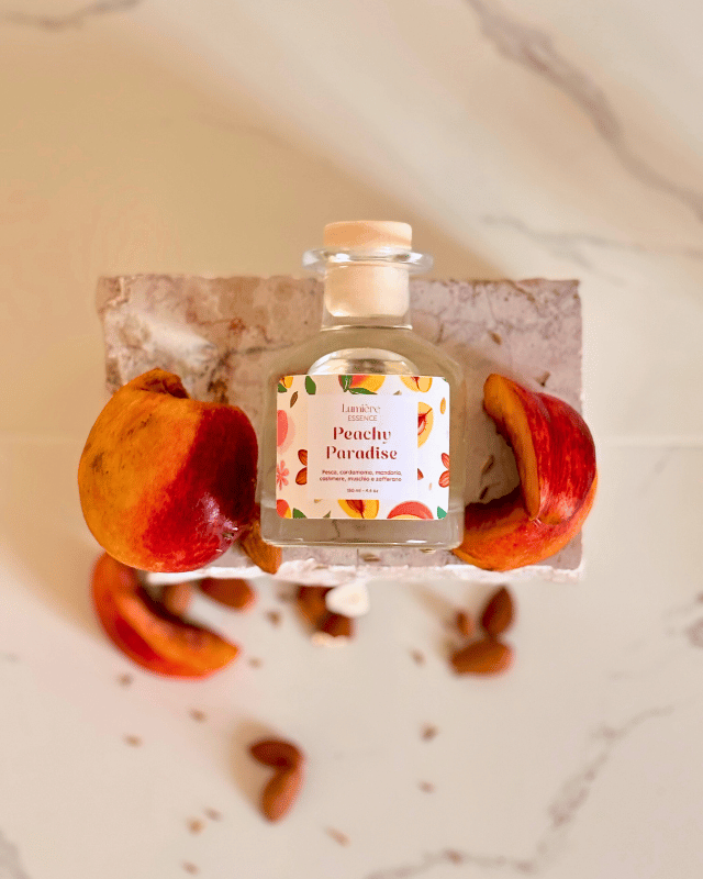 Diffusore per ambiente a bastoncino in bottiglietta di vetro su pietra di marmo e pesche che rappresentano la fragranza ripresa dall'alto