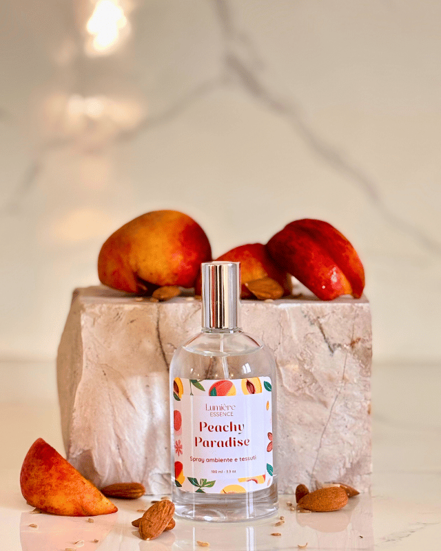 Spray per tessuti e ambiente in bottiglietta di vetro sullo sfondo pietra di marmo e pesche che rappresentano la fragranza