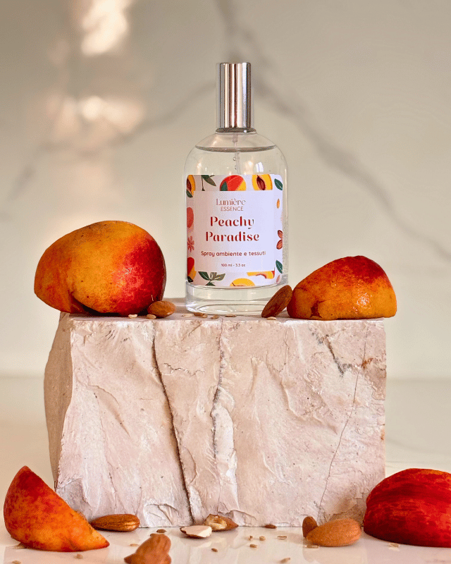 Spray per tessuti e ambiente in bottiglietta di vetro su pietra di marmo e pesche che rappresentano la fragranza