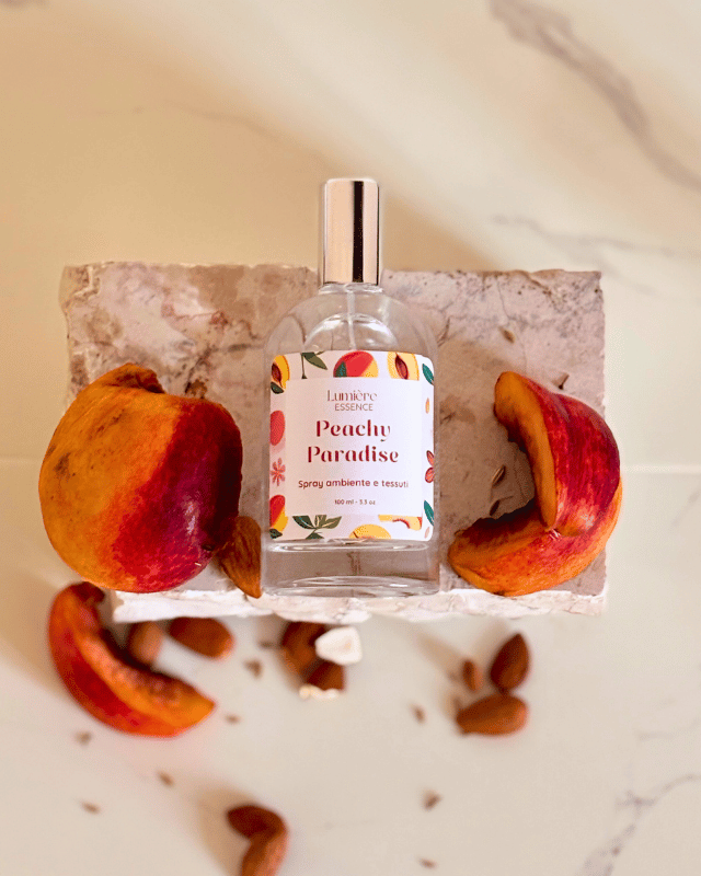 Spray per tessuti e ambiente in bottiglietta di vetro su pietra di marmo e pesche che rappresentano la fragranza