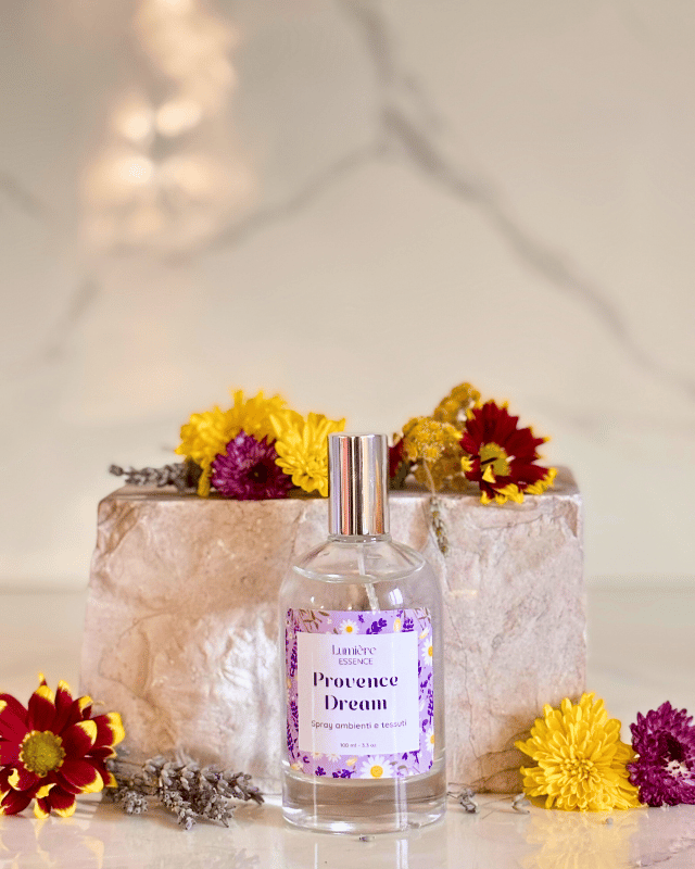 Spray per tessuti e ambiente in bottiglietta di vetro sullo sfondo pietra di marmo con fiori che rappresentano la fragranza