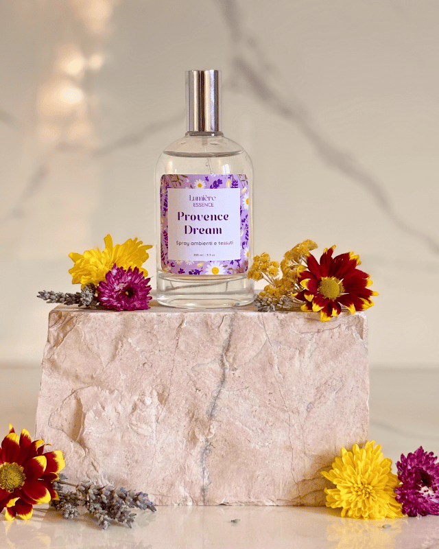 Spray per tessuti e ambiente in bottiglietta di vetro su pietra di marmo con fiori che rappresentano la fragranza