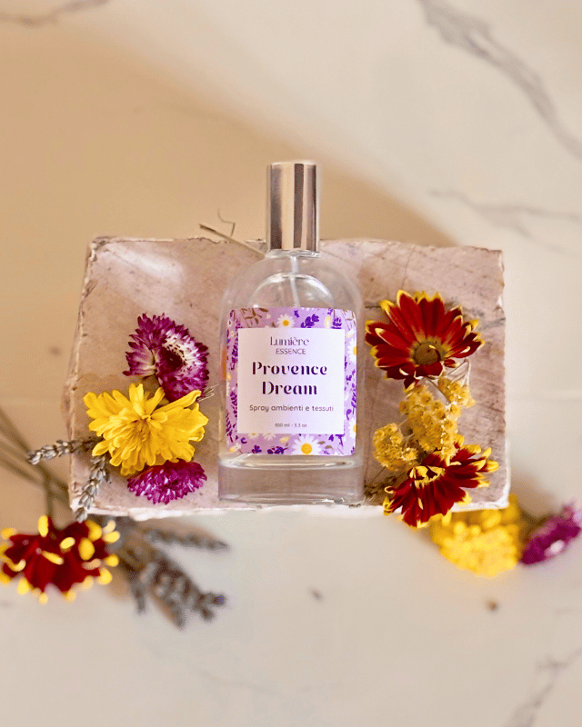 Spray per tessuti e ambiente in bottiglietta di vetro su pietra di marmo con fiori che rappresentano la fragranza vista all'alto