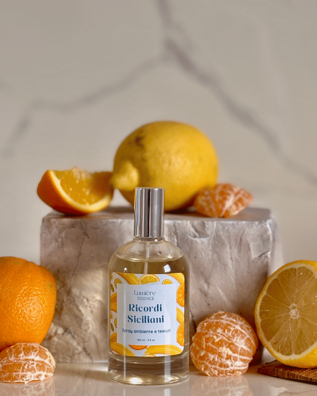 Spray per ambienti e tessuti in bottiglietta di vetro sullo sfondo limone arance e mandarino che rappresentano la fragranza