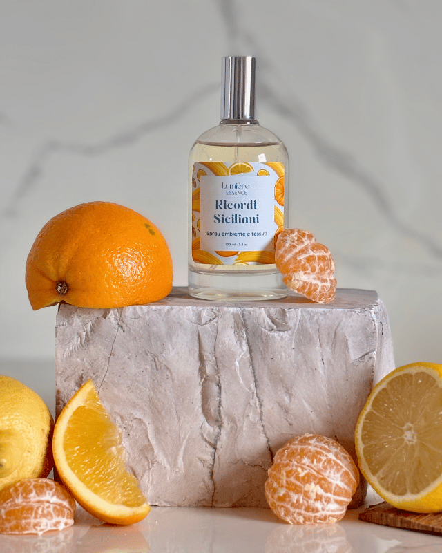 Spray per ambienti e tessuti in bottiglietta di vetro sullo sfondo limone arance e mandarino che rappresentano la fragranza su pietra di marmo