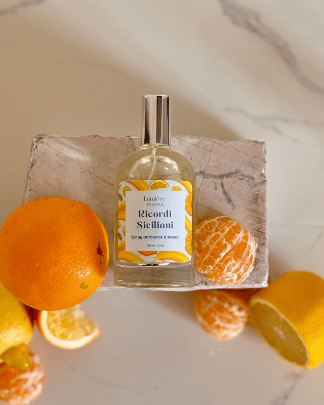 Spray per ambienti e tessuti in bottiglietta di vetro sullo sfondo limone arance e mandarino che rappresentano la fragranza su pietra di marmo vista dall'alto