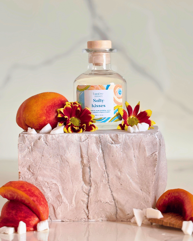 Diffusore a bastoncino in bottiglietta di vetro su pietra di marmo sullo sfondo pesche e scaglie di cocco 