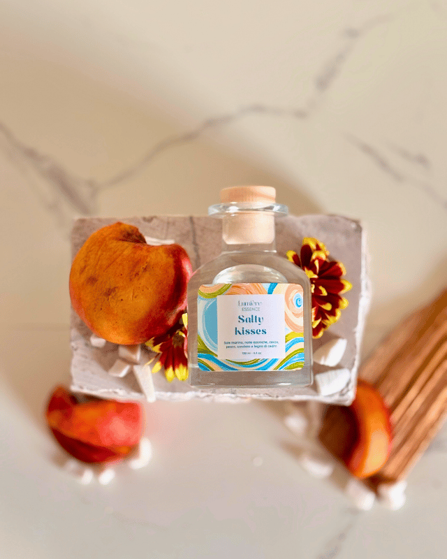 Diffusore a bastoncino in bottiglietta di vetro su pietra di marmo sullo sfondo pesche e scaglie di cocco