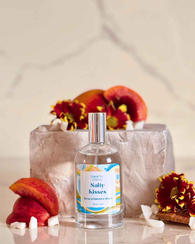 Spray per tessuti e ambiente in bottiglietta di vetro con pesche e fiori sullo sfondo una pietra di marmo