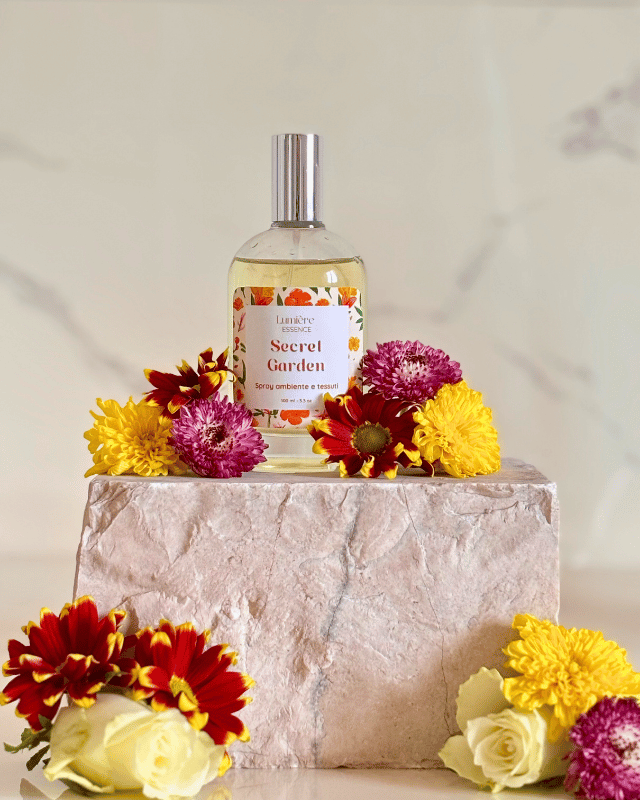 Spray in bottiglietta di vetro  profuma ambiente e tessuti sullo sfondo fiori  che rappresentano il profumo floreale su pietra di marmo