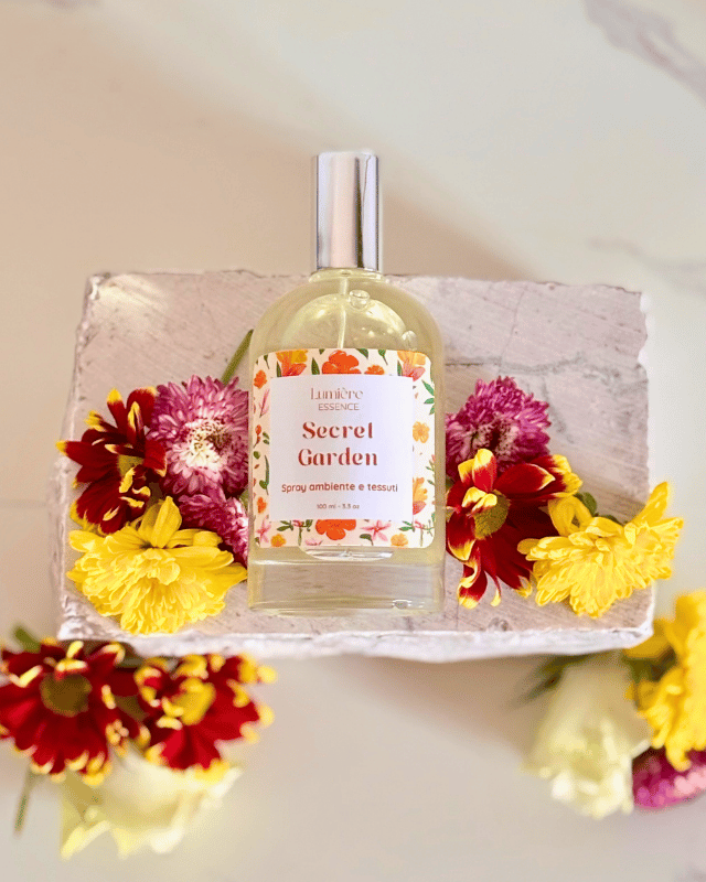 Spray in bottiglietta di vetro  profuma ambiente e tessuti sullo sfondo fiori  che rappresentano il profumo floreale su pietra dall'alto 