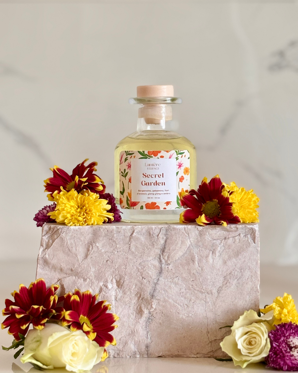 Diffusore a bastoncino in bottiglietta di vetro su pietra di marmo con fiori freschi che rappresentano la fragranza