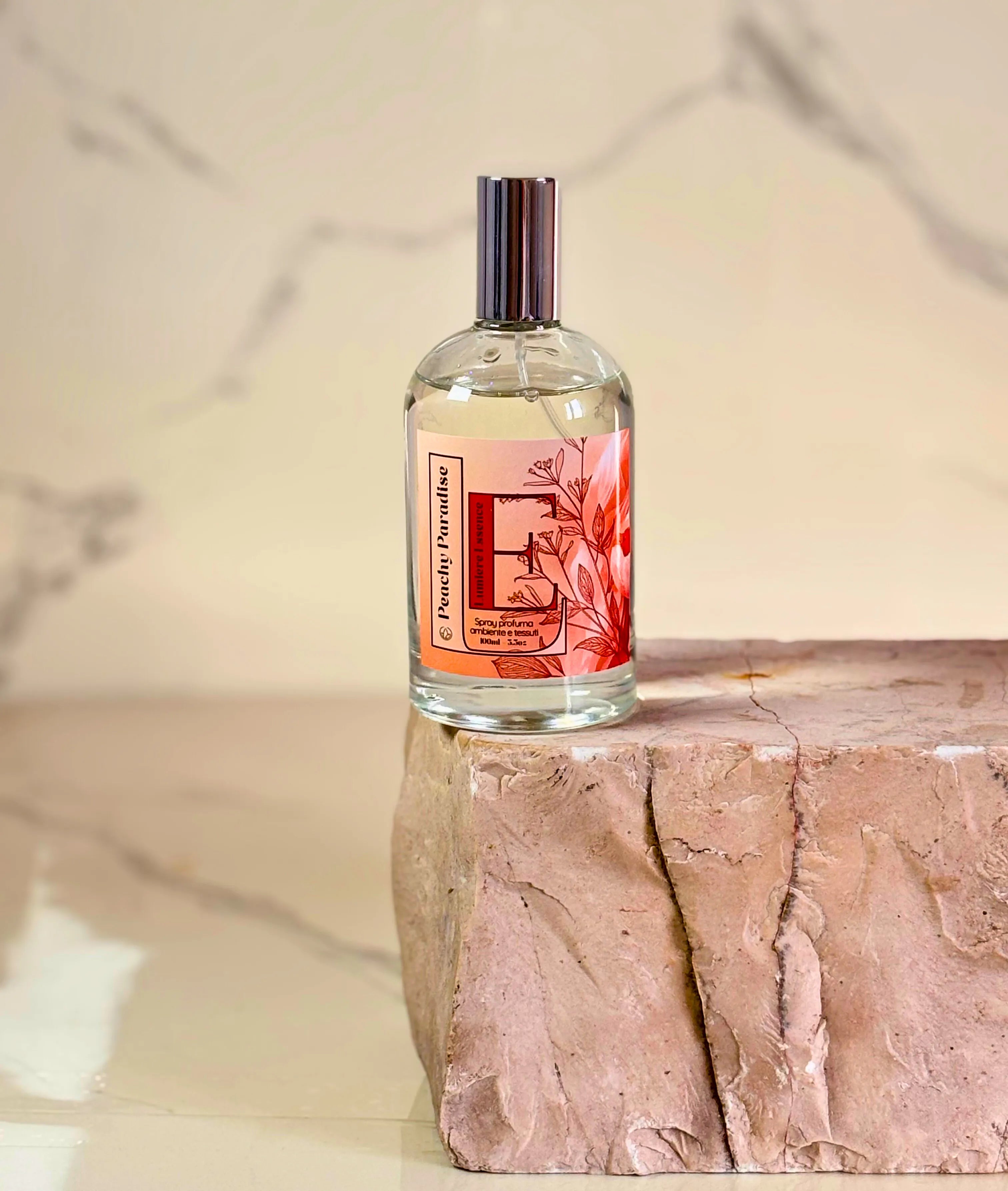 Flacone di spray profumo ambiente e tessuti Peachy Paradise, 100ml, sullo sfondo di tessuti colorati.