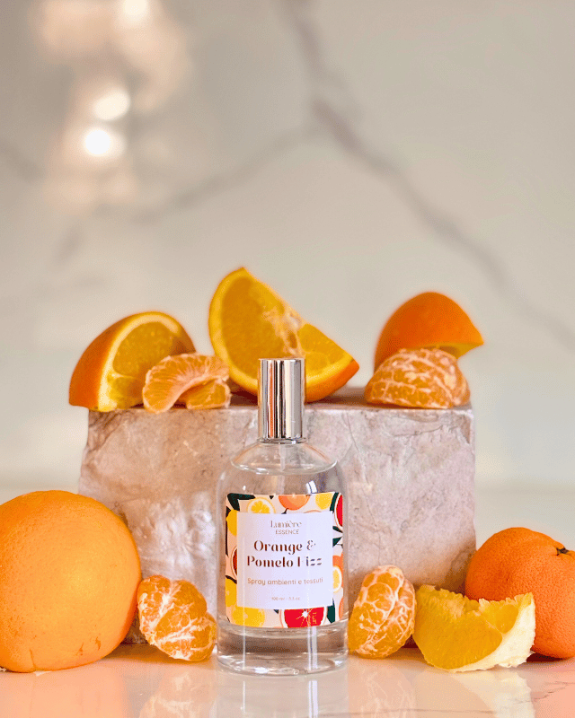 Spray profuma ambiente e tessuti in bottiglietta di vetro sullo sfondo arance pompelmo e mandarino e pietra di marmo, la frutta rappresenta la fragranza