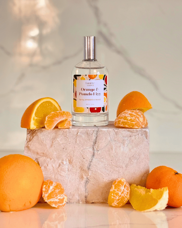 Spray profuma ambiente e tessuti in bottiglietta di vetro sullo sfondo arance pompelmo e mandarino su pietra di marmo, la frutta rappresenta la fragranza
