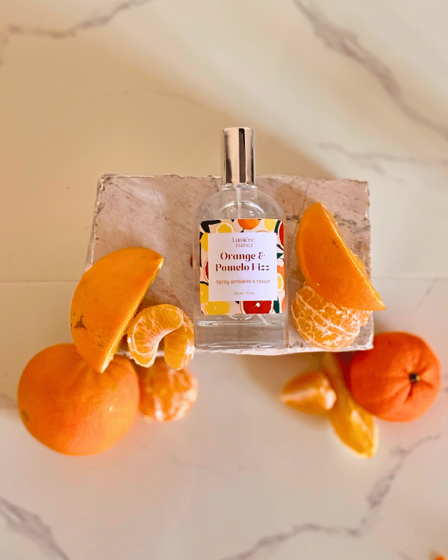 Spray profuma ambiente e tessuti in bottiglietta di vetro sullo sfondo arance pompelmo e mandarino su pietra di marmo, la frutta rappresenta la fragranza